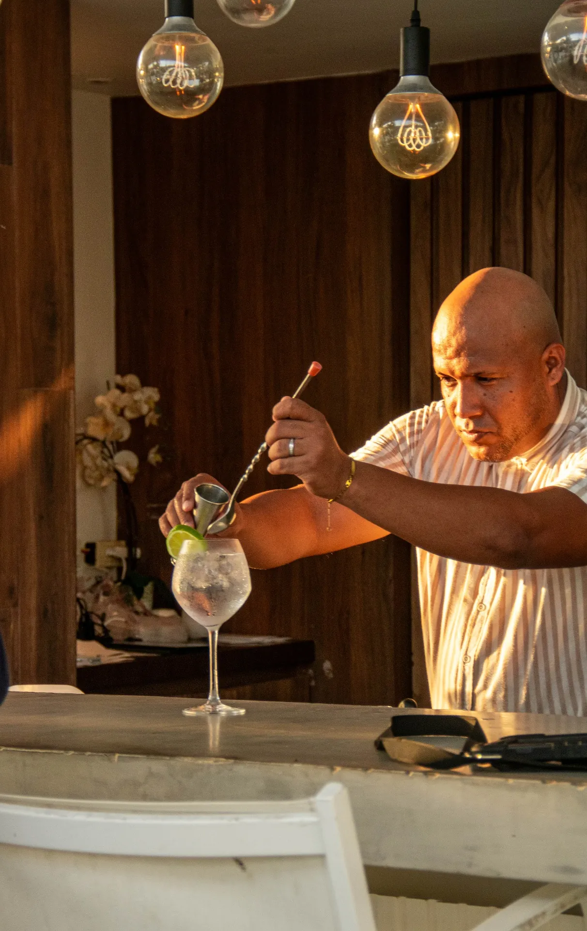 Bartender preparando coctel bajo luz cálida de bombillos